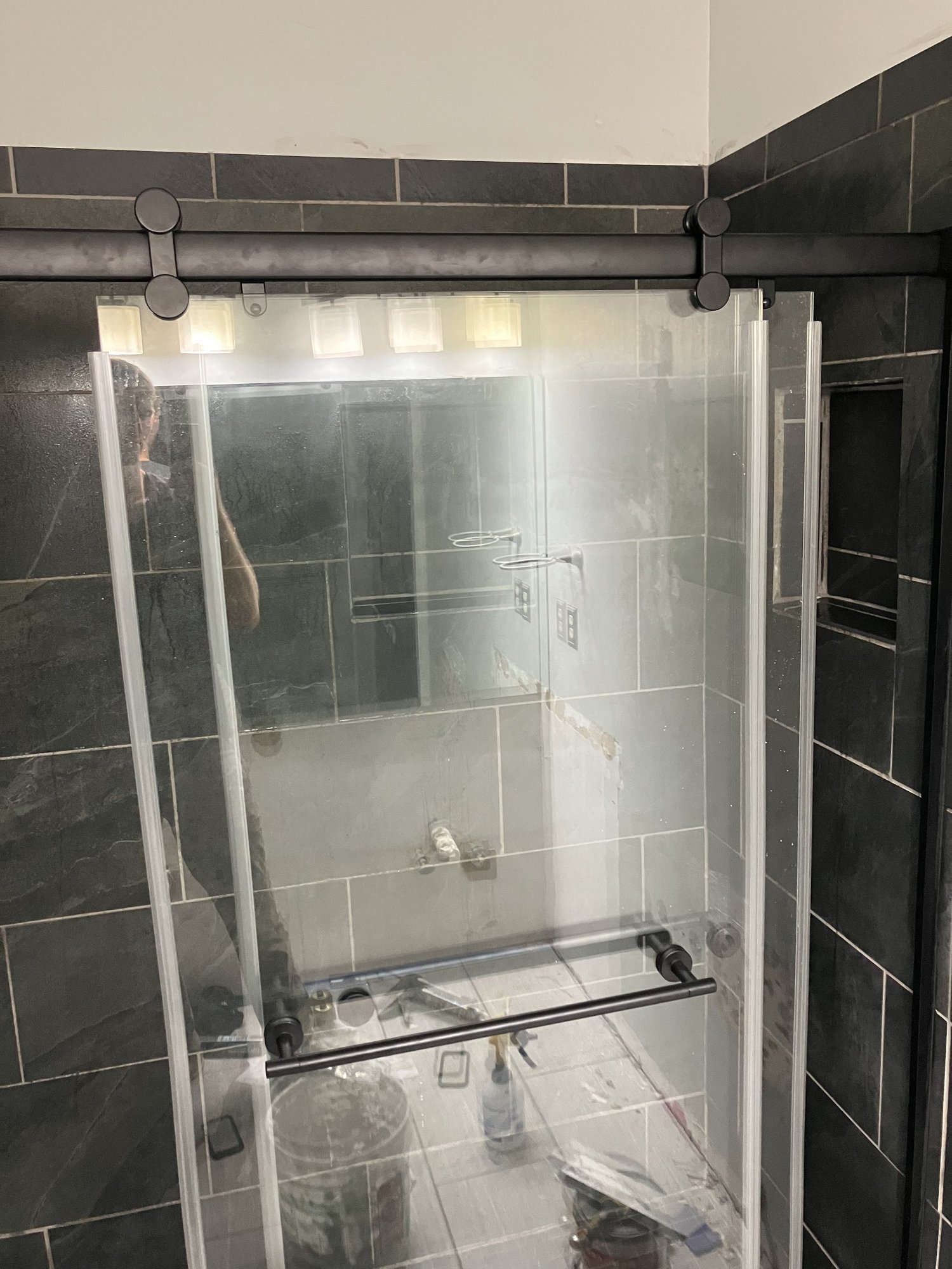 A custom bathroom with a sliding glass shower door and dark tile, still in the last stretch of the job.