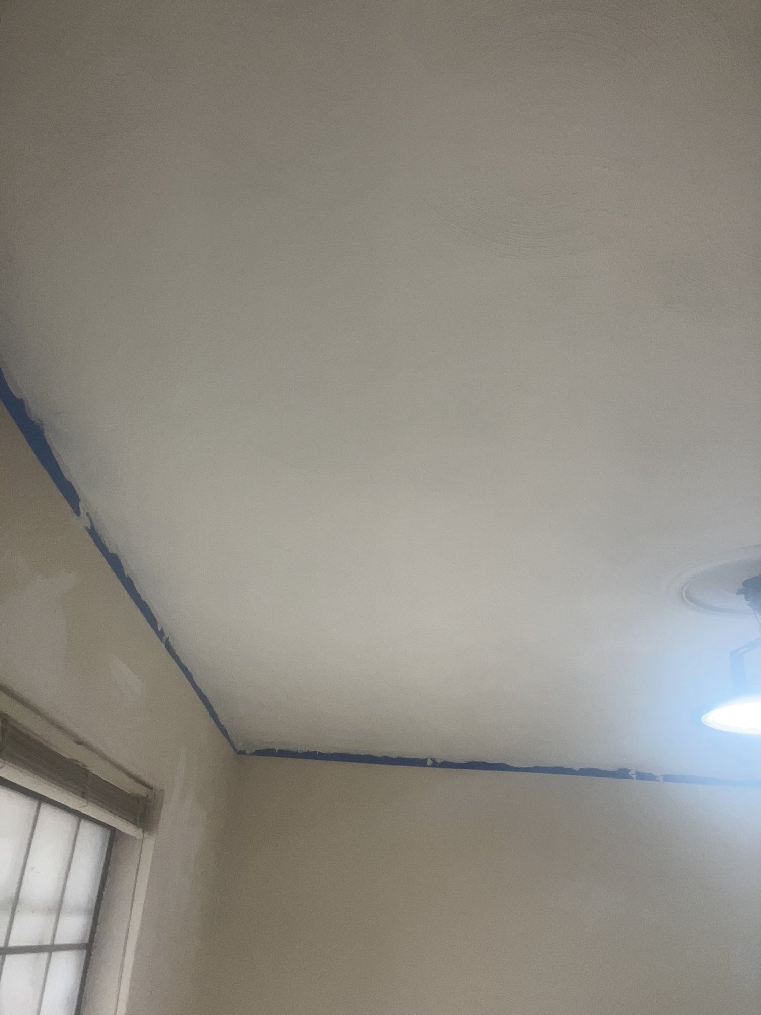 A ceiling after drywall and paint, blue tape still on the corners.