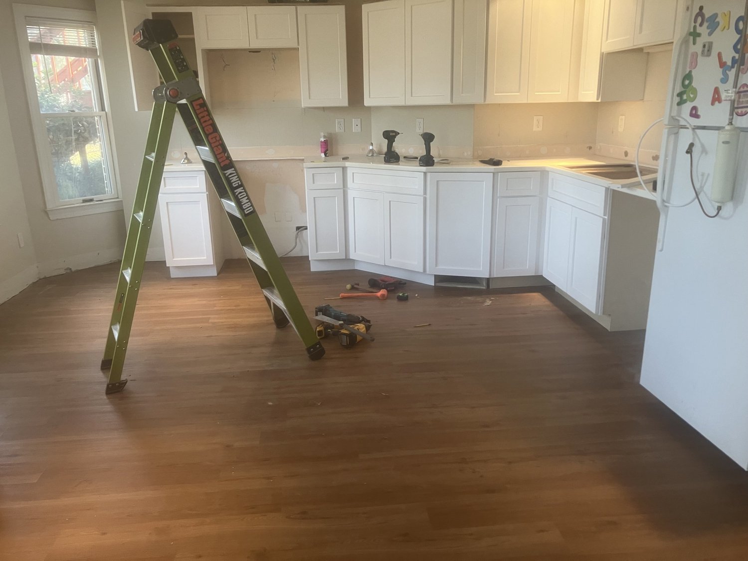 New wood-look flooring in a kitchen, tools and a ladder still on the job.